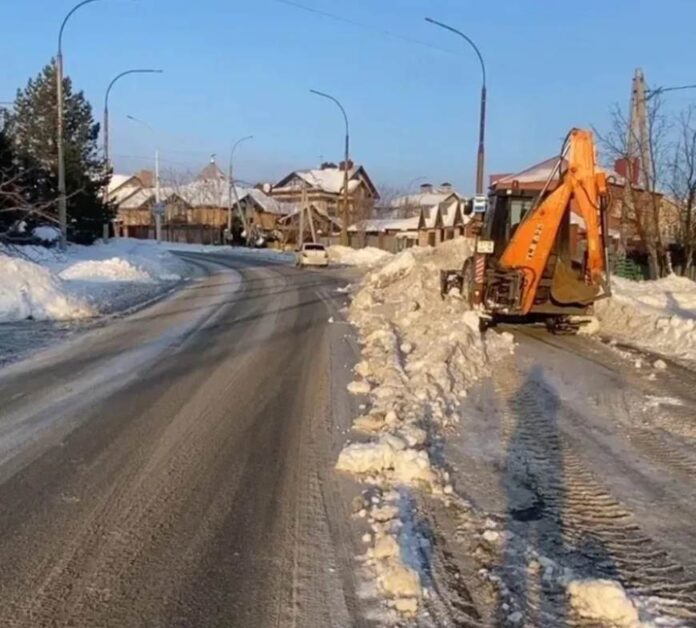 Спецтехника сгребает снег на городской улице , идет уборка снега в Оренбурге